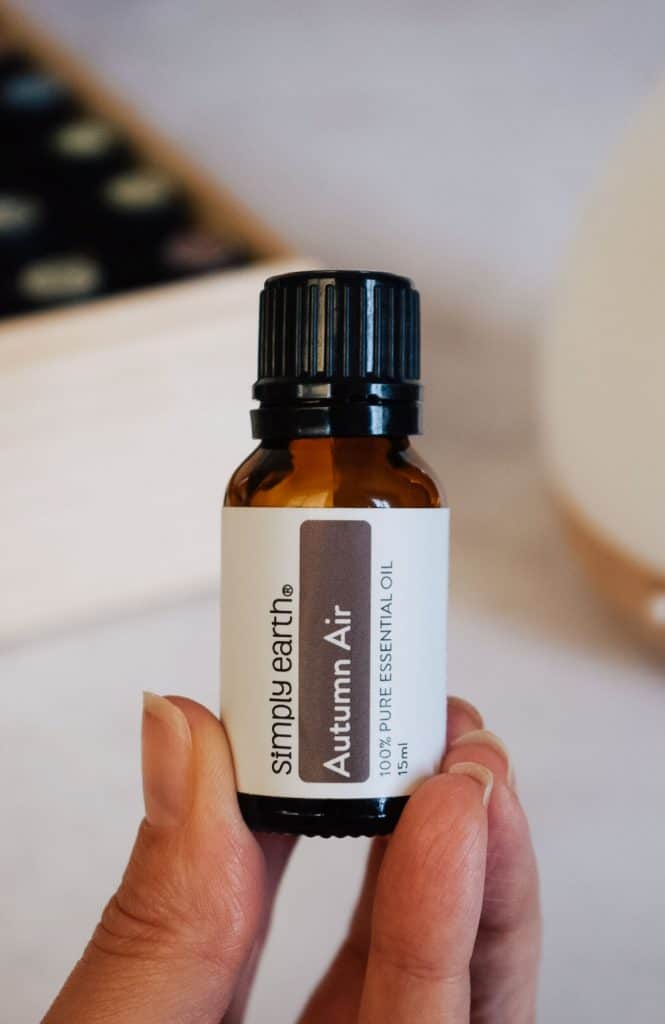 Person holding bottle of Autumn Air Simply Earth essential oil blend.