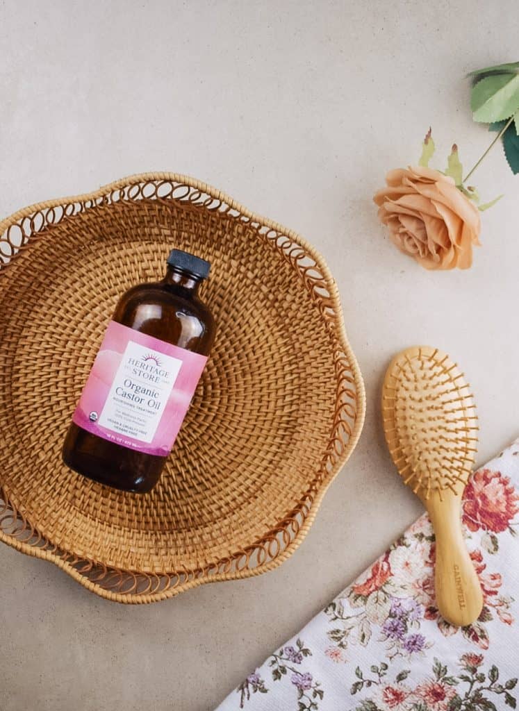 A bottle of castor oil in a rattan basket beside a floral dish towel and a hairbrush.