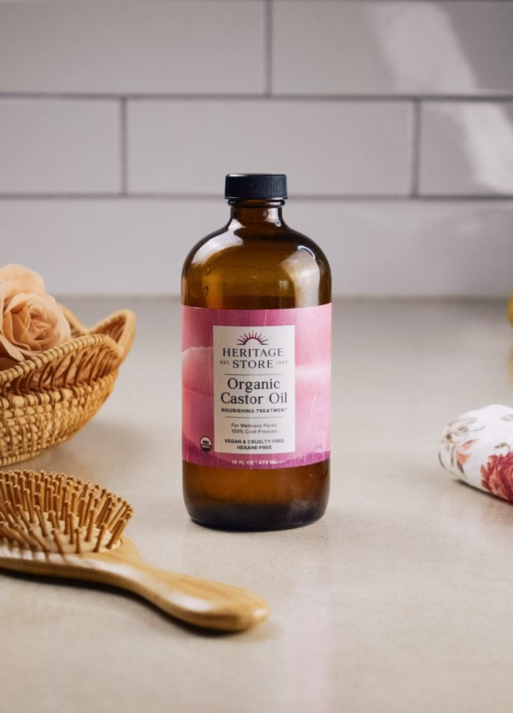 A bottle of castor oil on the kitchen counter beside a floral dish towel and a hairbrush.