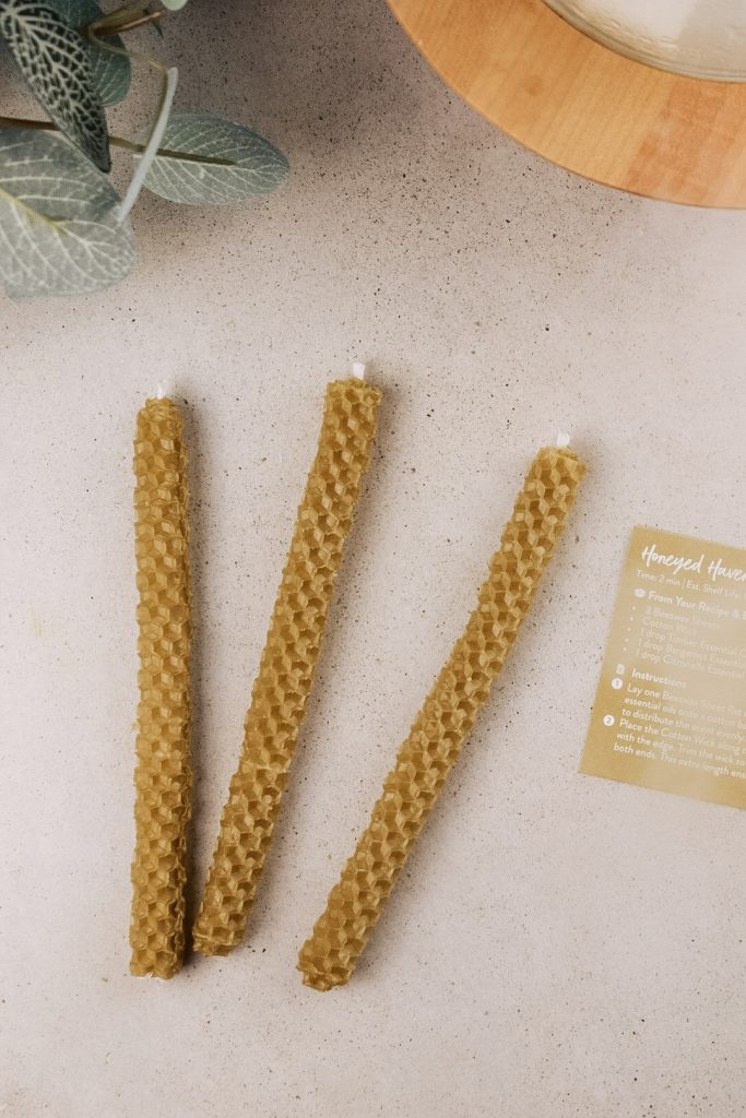Homemade beeswax candles are displayed on the counter next to a plant and an essential oil diffuser.